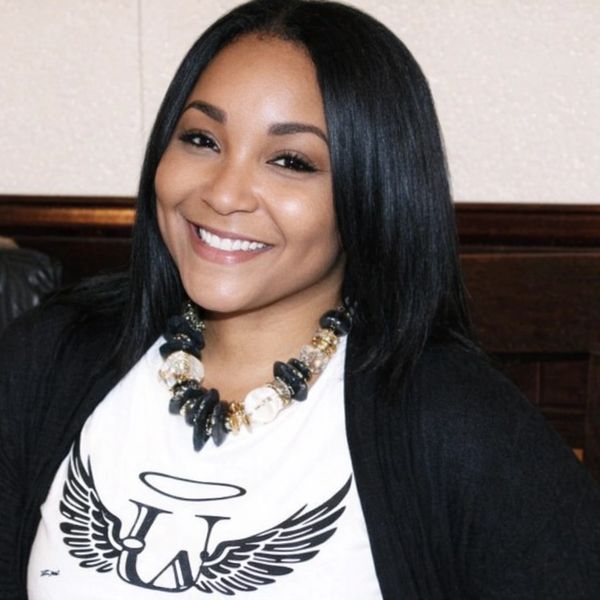 Smiling woman with straight black hair wearing a white graphic tee and statement necklace.