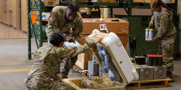 Three soldiers inspecting equipment in a warehouse.