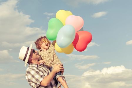 Dad holding son who is holding balloons with both of them smiling