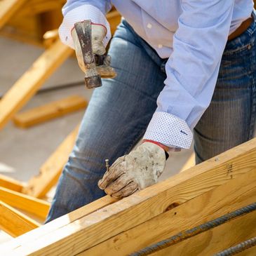 Person hammering a nail into wooden planks wearing gloves and casual clothes.