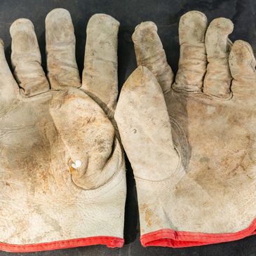 Worn leather gloves with red cuffs, showing signs of heavy use.