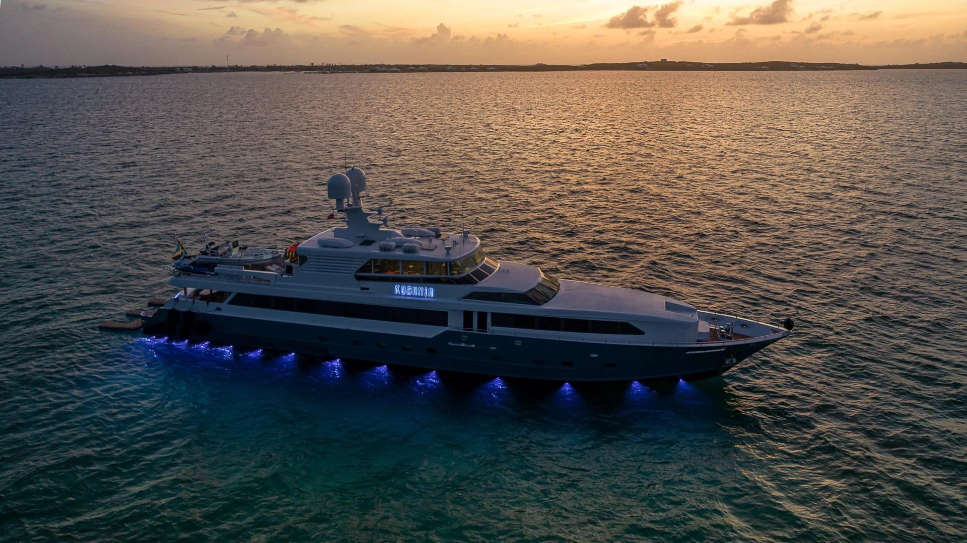 Luxury yacht glowing with blue lights at sunset on calm waters.