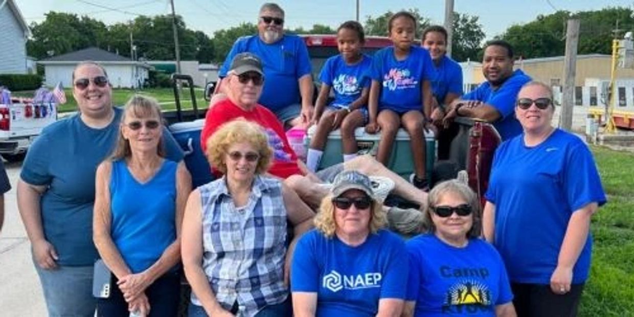 Group of people posing outdoors, some seated on a truck bed.