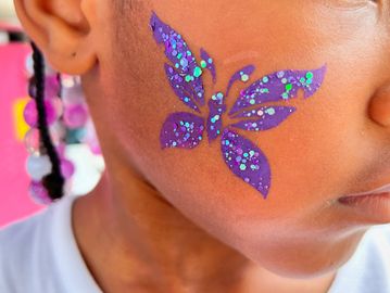 Child with a purple glittery butterfly face paint on their cheek.