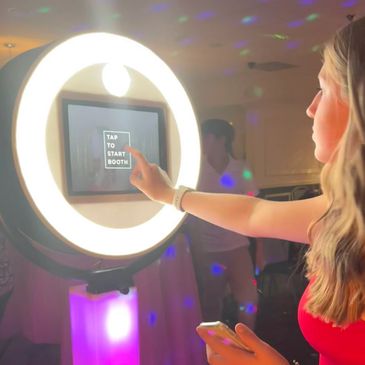 A young woman uses a photo booth with colorful lights around her.