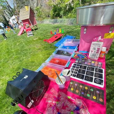 Colorful outdoor party setup with sand art, face painting, and games on a sunny day.