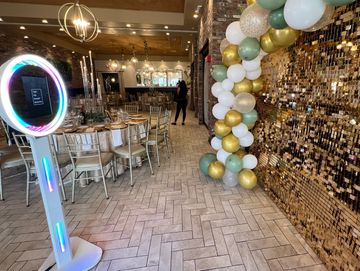 Elegant event setup with gold, white, and green balloons and a sparkling photo booth.