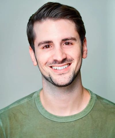 Smiling young man with dark hair wearing a green shirt.