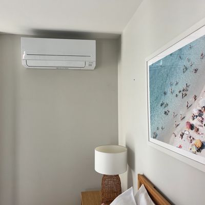 Modern bedroom corner with air conditioner, lamp, and beach photo.