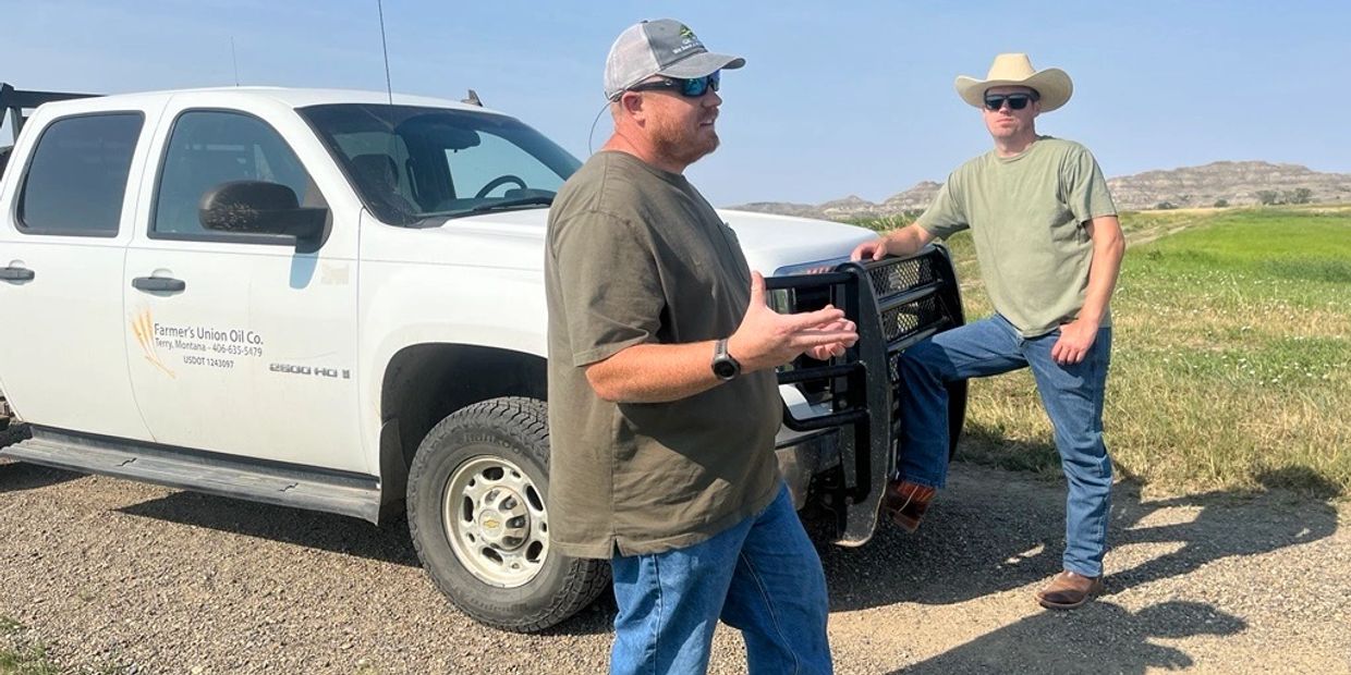 Two men talking by a white truck in a rural area.
