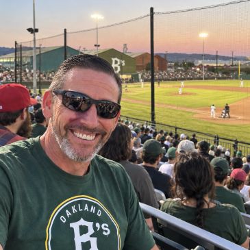 Smiling man at a baseball game during sunset.