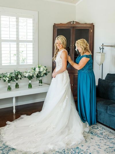 Mother of the bride helping a bride get into her dress. Mother of the bride dress had alterations