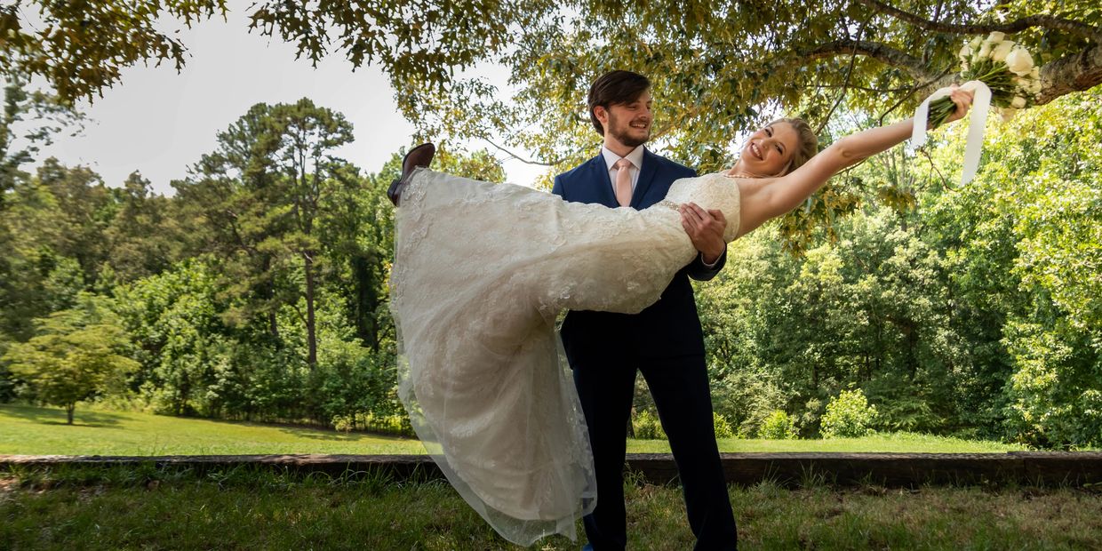 Groom holding bride in a joyful outdoor wedding moment.