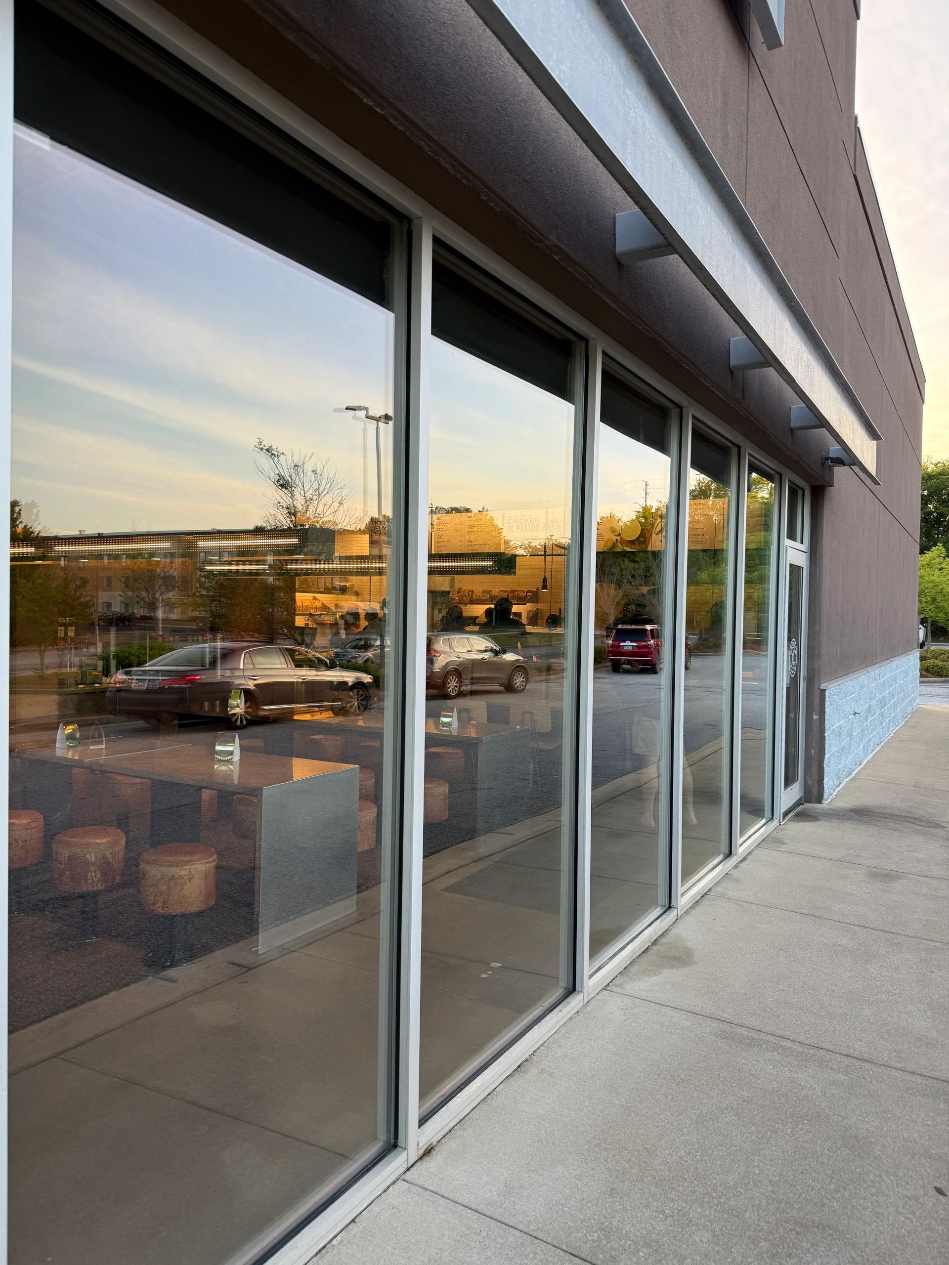 Reflection of cars and sky on large restaurant windows at sunset.