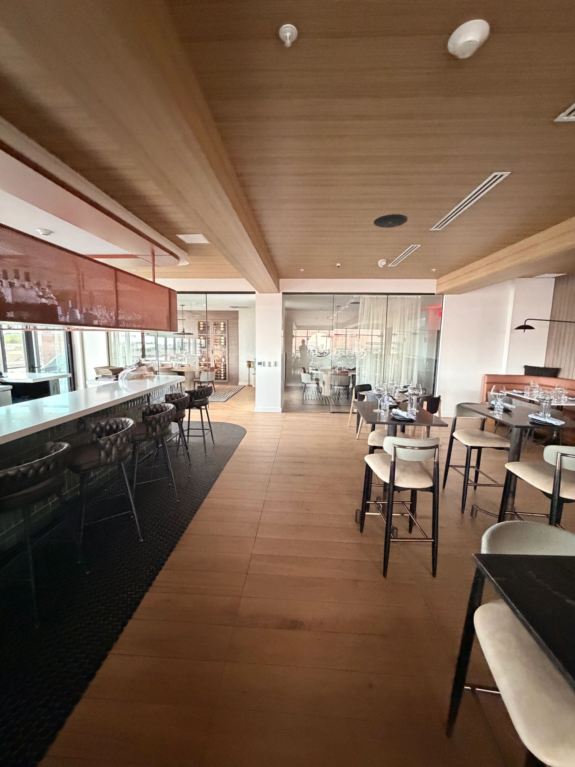 Modern restaurant interior with bar seating and glass-enclosed dining area.