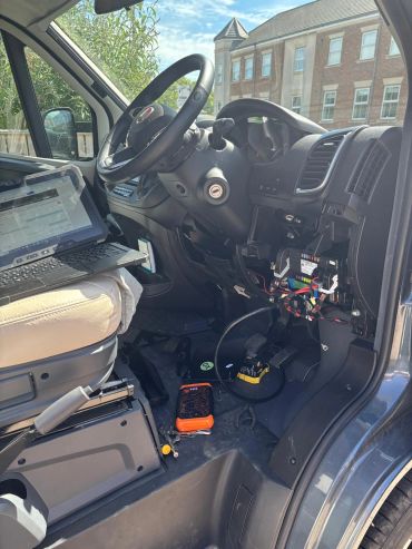 Interior of a vehicle with the dashboard panel removed and devices connected.