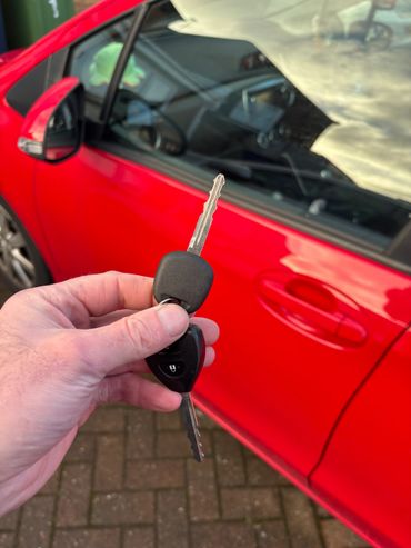 Hand holding a car key in front of a red car door.