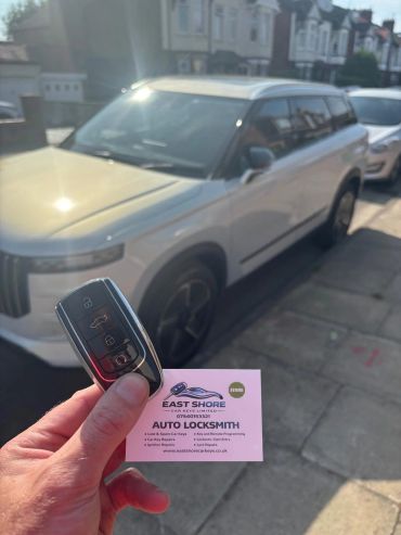 Hand holding car key and locksmith business card in front of a white SUV.