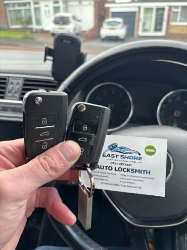 Hand holding two car keys and a locksmith business card inside a car.