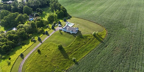 An aerial view of a house and green farm fields and a driveway approaches the house