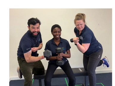 Three people posing with dumbbells, smiling and flexing muscles indoors.
