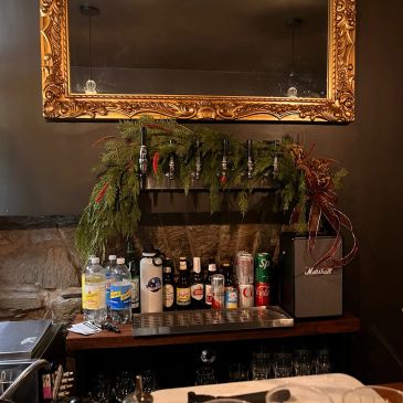 Bar shelf with beer taps and bottles under a gold frame mirror.
