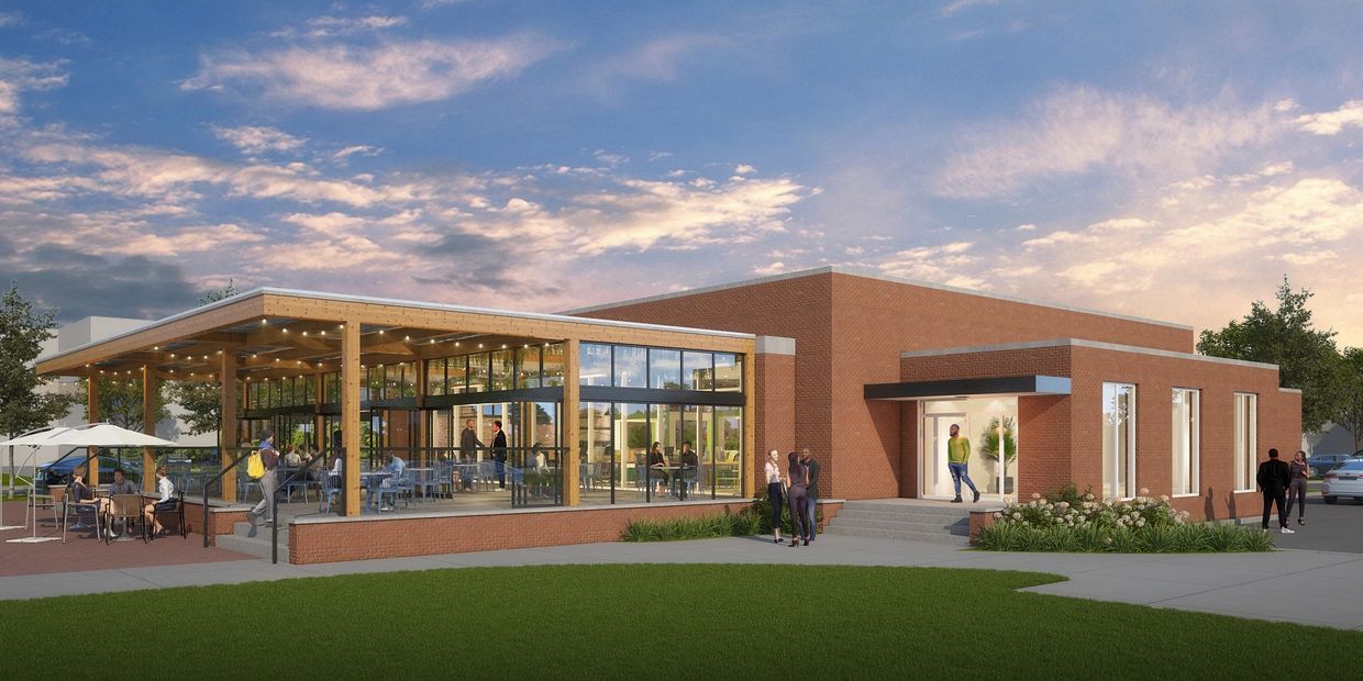 Modern brick building with outdoor seating and glass walls under a partly cloudy sky.
