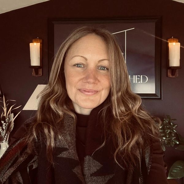 Smiling woman with long wavy hair indoors with lit candles.