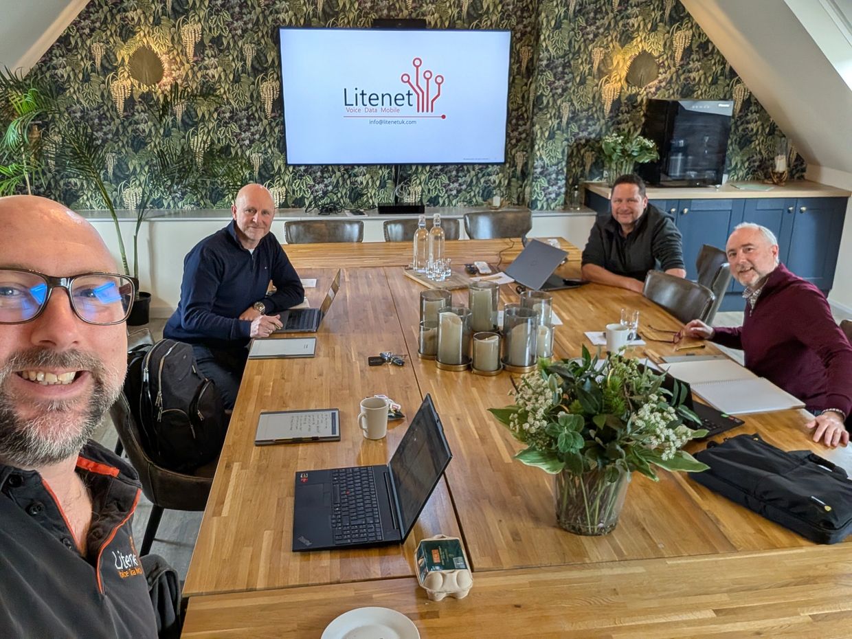 Four men in a meeting room with laptops and a screen showing Litenet.