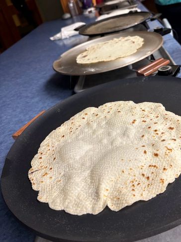 Flatbreads cooking on pans lined up on a countertop.