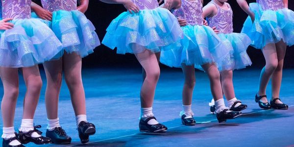 Children performing tap dance on stage in blue skirts.
