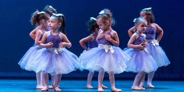 Young girls in purple ballet tutus dancing on stage.