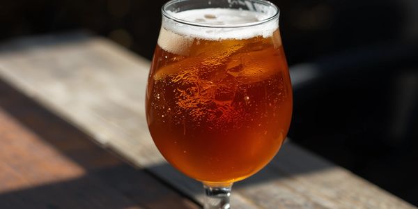 A glass of amber beer with a foamy head on a wooden table.