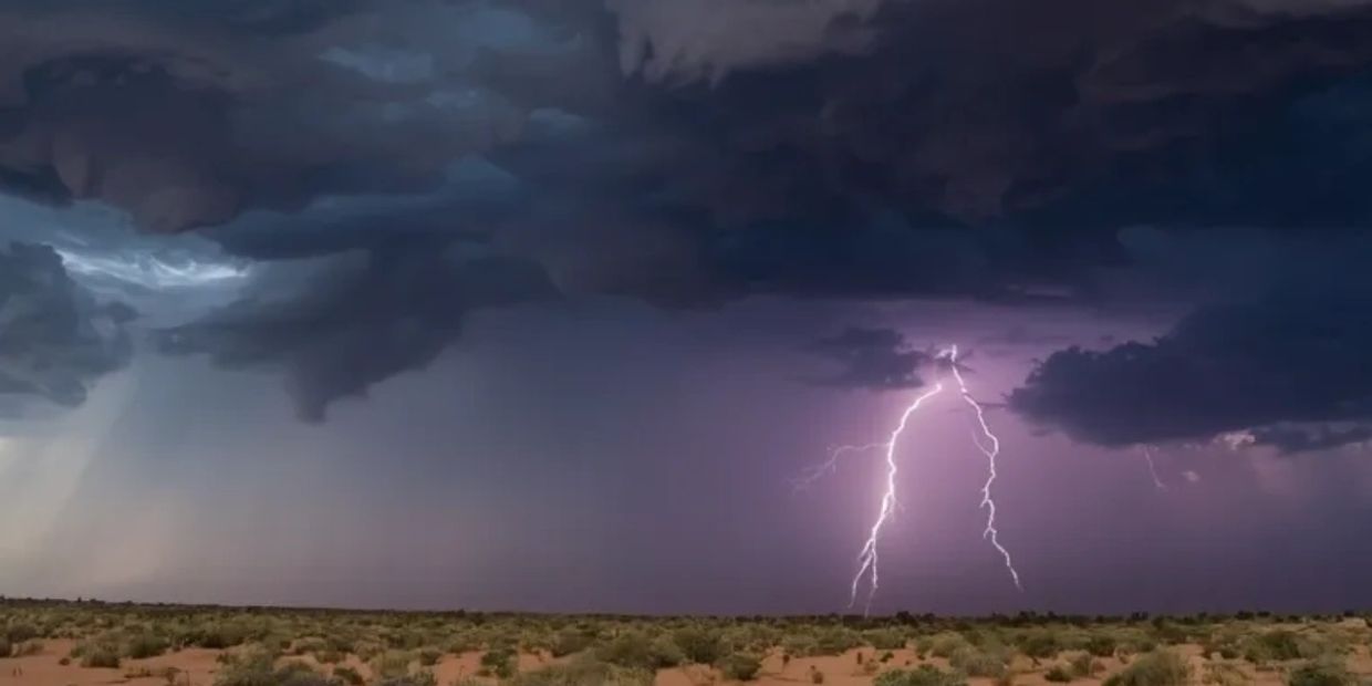Lightning strikes during a storm over a desert landscape under dark clouds.