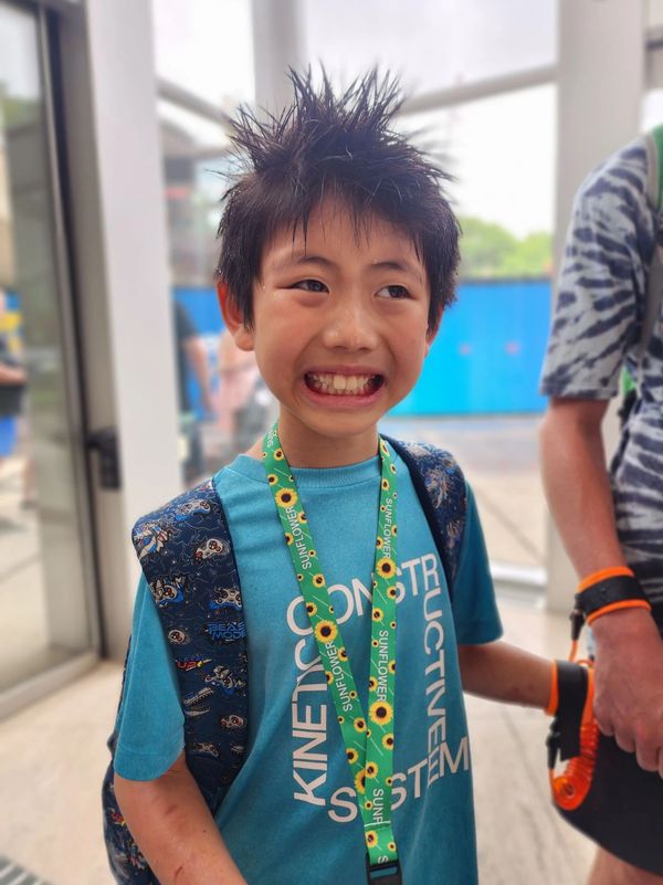 Smiling boy with spiky hair wearing a blue shirt and sunflower lanyard.