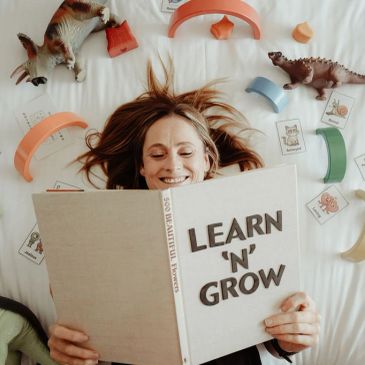 Woman reading a book titled 'Learn 'N' Grow' surrounded by dinosaur toys and educational cards.
