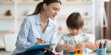 A woman observing a child playing with colorful blocks.