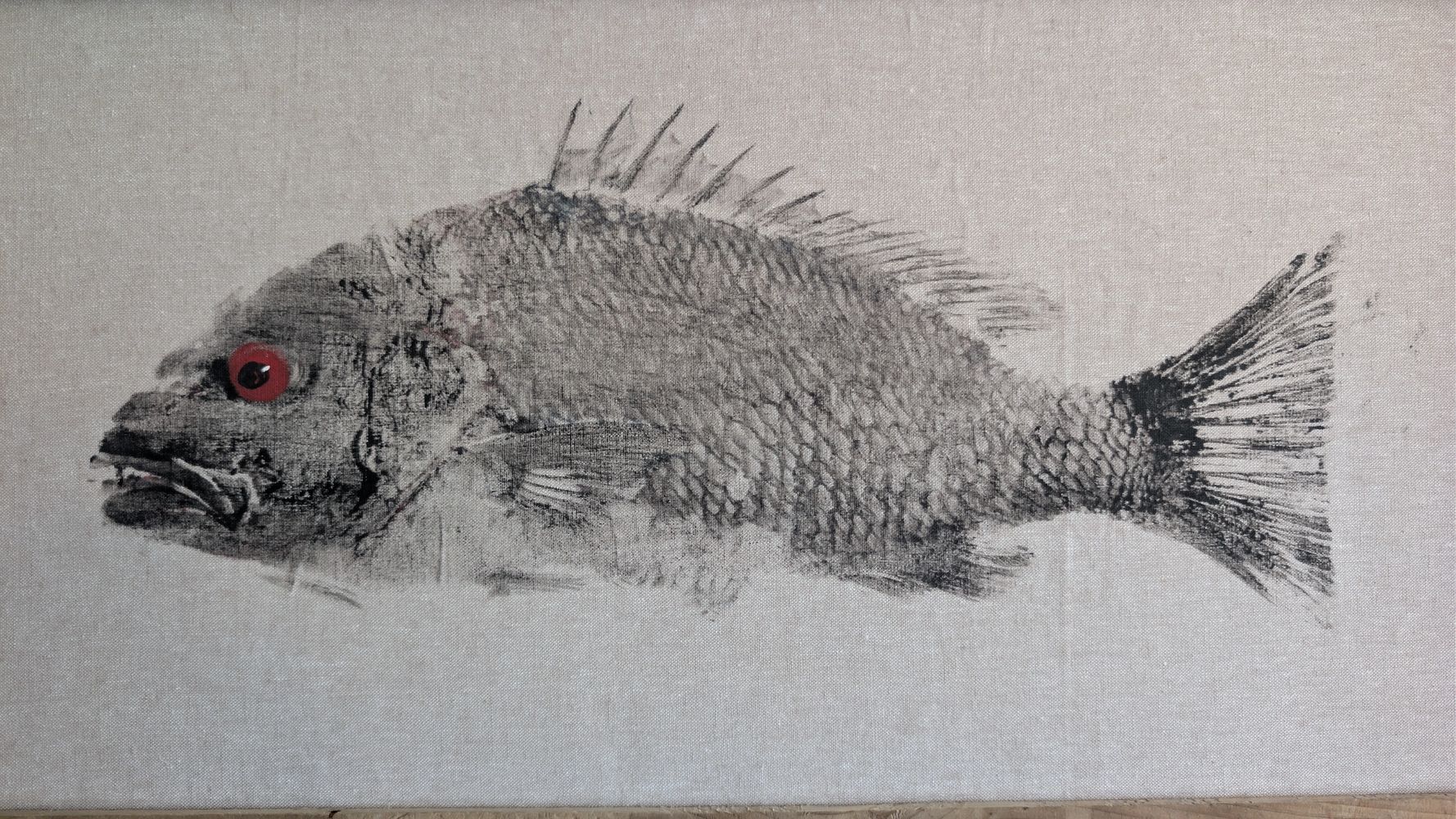 Detailed fish print with a striking red eye on a neutral fabric background.