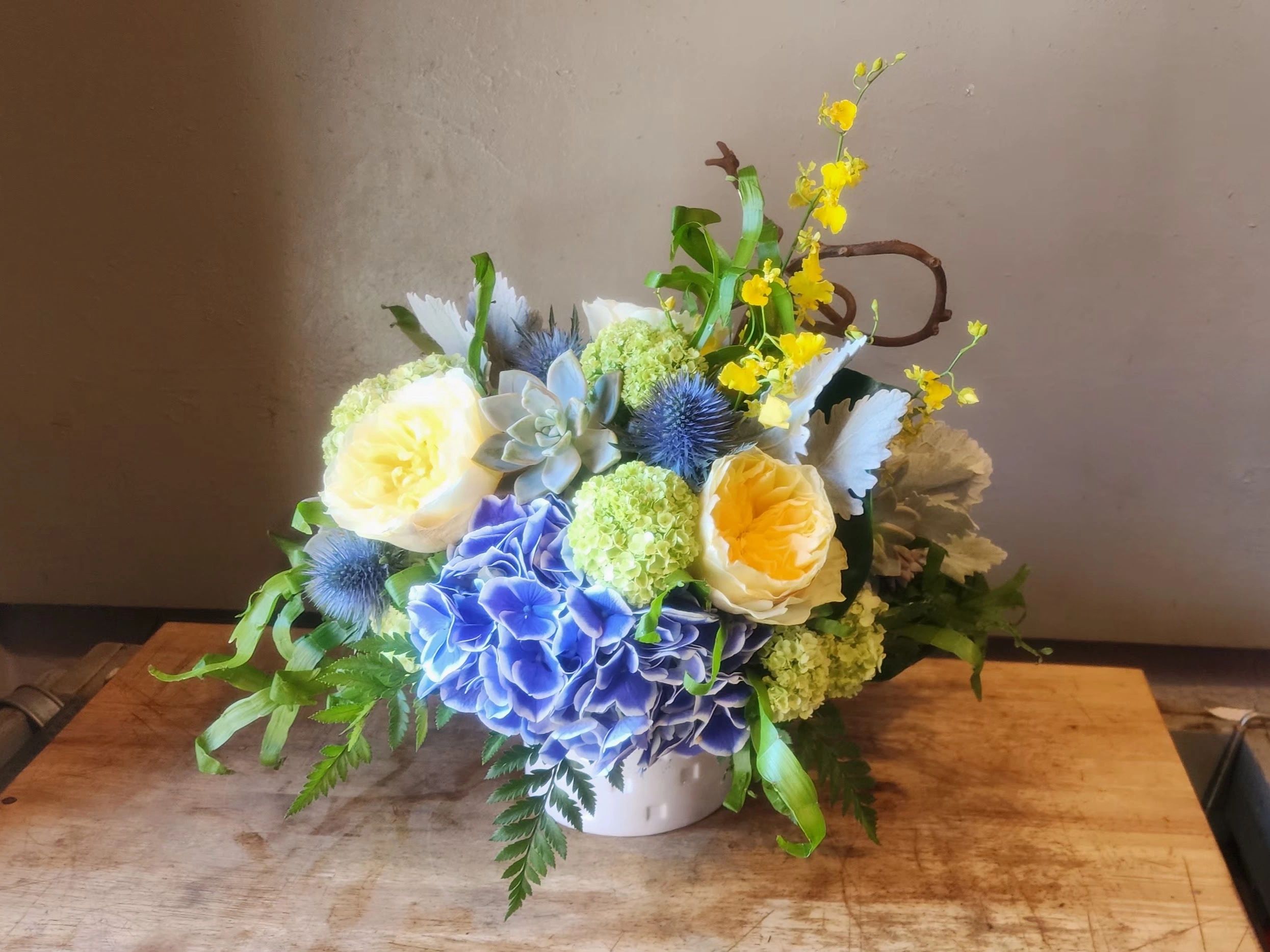 A radiant mix of yellow garden roses, blue hydrangea, orchids, and succulents inspired by the Greek 