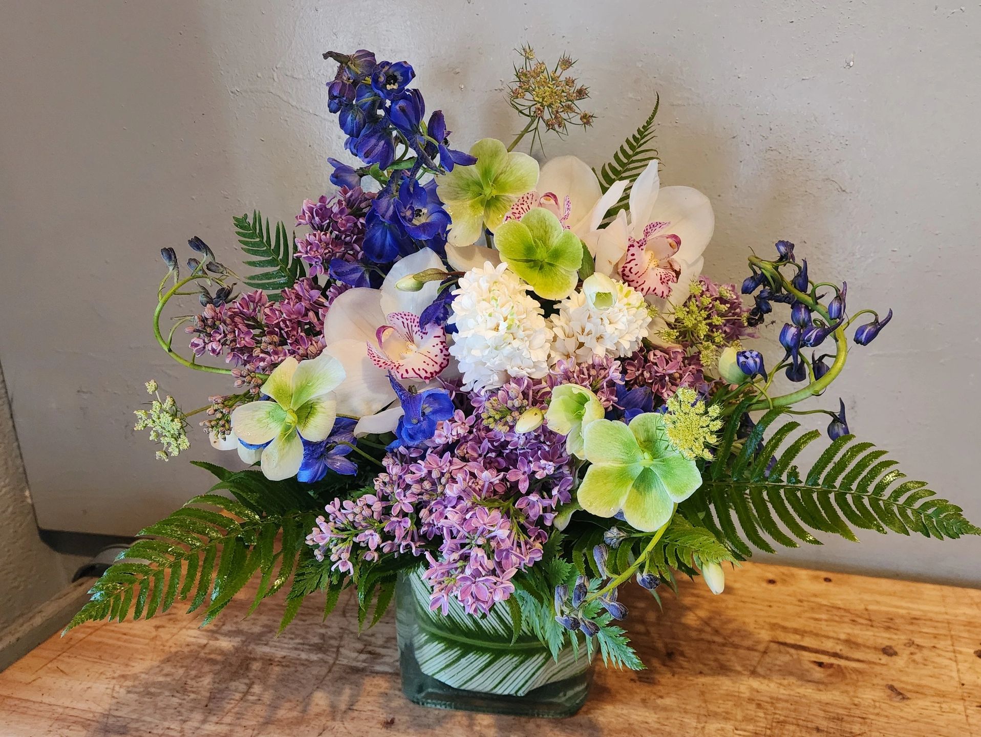 Apollo's Celestial Symphony, made with white cymbidiums, lilac, hellebores, blue delphiniums.
