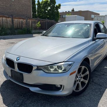 Silver BMW sedan parked in an outdoor lot with headlights on.