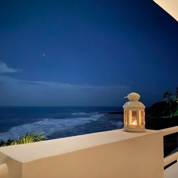 A well-lit lantern on the edge of a balcony on a starry night by the ocean