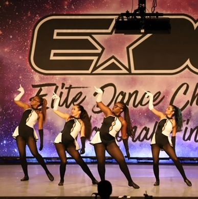 Four dancers performing a synchronized routine on stage in black and white costumes.