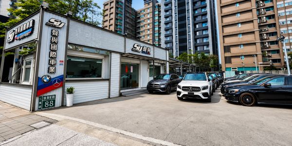 Car dealership with luxury vehicles parked outside near tall buildings.