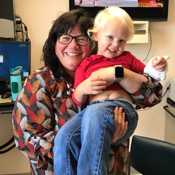 Smiling doctor hugging blonde toddler. 