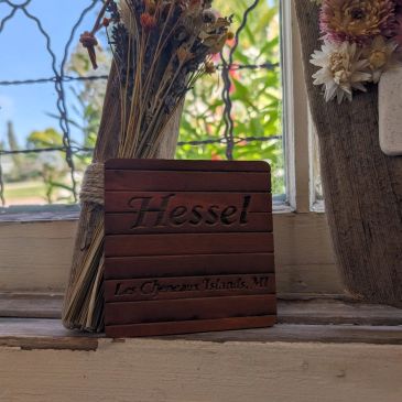 Wooden nameplate with dried flowers by a window.
