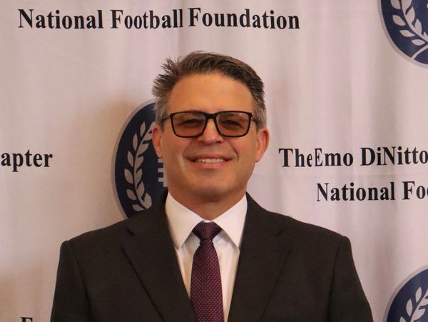 Man in suit and glasses smiles at a National Football Foundation event.