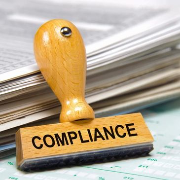 Wooden stamp labeled 'COMPLIANCE' on paperwork.