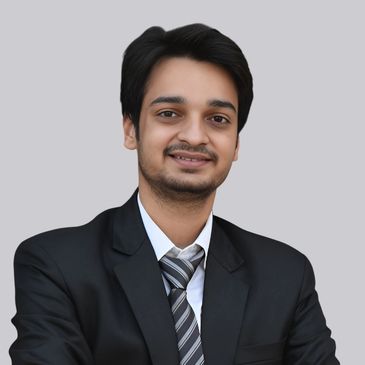 Young man in a black suit smiling confidently against a plain background.