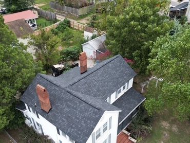 Aerial view of a white house with a newly installed dark roof surrounded by trees.